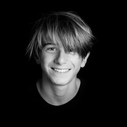 Portrait of smiling teenage boy against black background