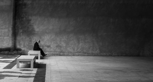 Rear view of woman sitting on bench against wall