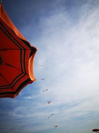 Low angle view of parasol and kites against sky