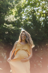 Low angle view of pregnant woman with hands on stomach standing in park