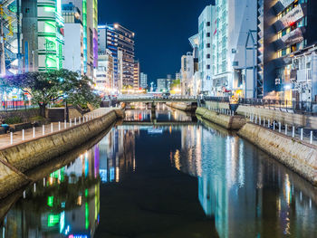 Reflection of illuminated bridge over river in city at night
