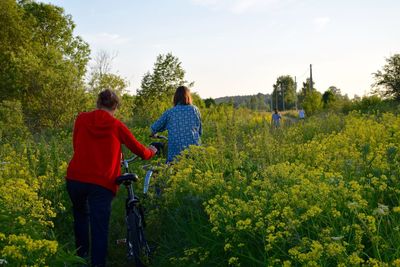 Rear view of friends with bicycle walking on field against sky