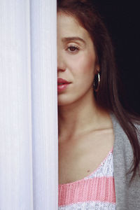 Close-up portrait of young woman behind curtain