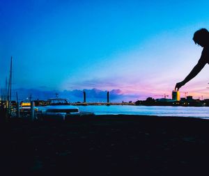 Silhouette city by sea against blue sky during sunset