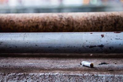 Close-up of cigarette butt by metallic pipes on footpath