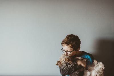 Boy kissing yorkshire terrier against wall at home