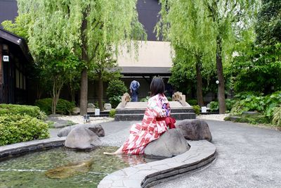 Rear view of woman relaxing on rock by pond against shrine