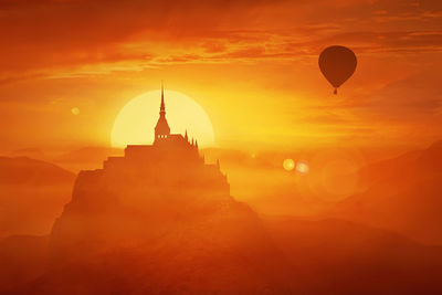 Silhouette of hot air balloons flying over a castle against sky during sunset