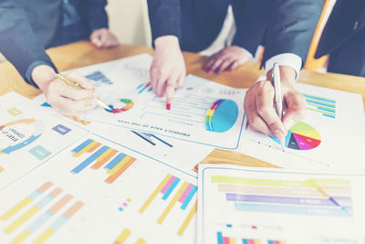 Midsection of colleagues analyzing charts on office desk