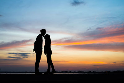 Silhouette man and woman standing against sky during sunset