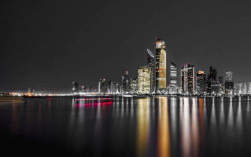 Illuminated buildings by river against sky at night