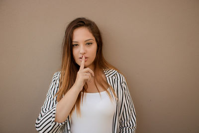 Portrait of young woman with finger on lips against brown background