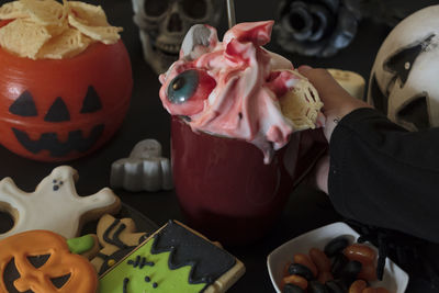 Woman holding mug with delicious halloween drink on decorated table with candy and snacks