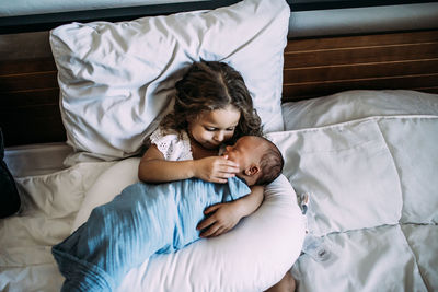 Young girl holding newborn baby brother on bed