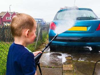 Rear view of boy washing car with high pressure cleaning