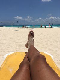 Low section of person relaxing on beach against sky