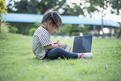 Side view of woman using mobile phone while sitting on grass