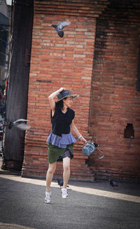 Full length of woman standing against brick wall