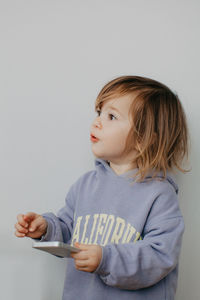 Portrait of cute girl using mobile phone while standing against wall