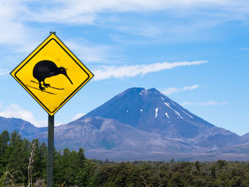 Yellow road sign by snowcapped mountain against sky