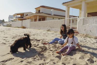 Side view of two girl playing with dog and sitting at the beach