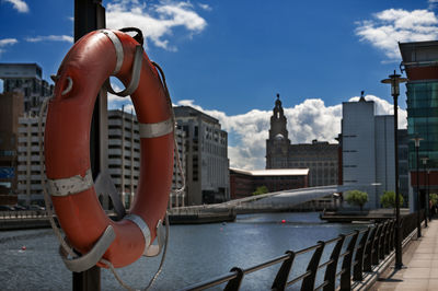 Life belt on pole by river against buildings and sky