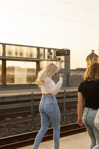 Rear view of woman standing by railroad tracks against sky