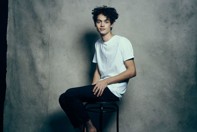 Portrait of young man sitting against wall