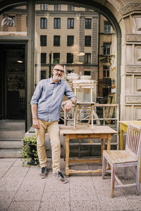 Smiling owner leaning on chair outside antique shop