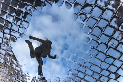 Reflection of woman jumping seen in puddle on street