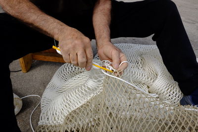 Low section of fisherman repairing fishing net on field