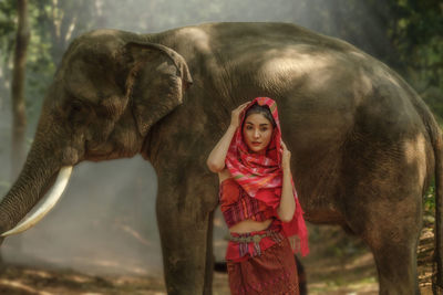 Beautiful woman in traditional costume standing with the big elephant in jungle