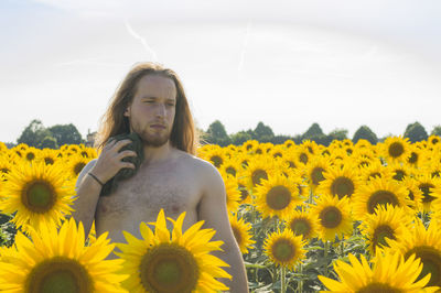 Thoughtful shirtless man wiping himself from towel while standing amidst sunflowers