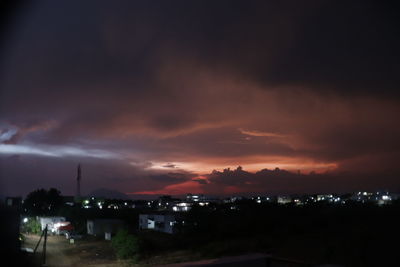 Illuminated city against dramatic sky at night