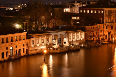 Boats moored on illuminated canal by buildings in city at night