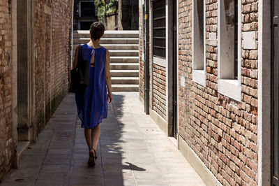 Rear view of woman walking on footpath amidst brick walls