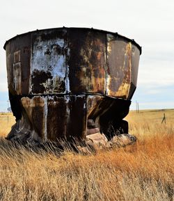Rusty damaged container on grassy field against sky