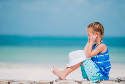 Side view of girl listening music sitting at beach