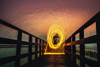 Man spinning wire wool on pier over lake against sky during sunset