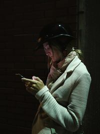 Woman wearing helmet while using mobile phone against building