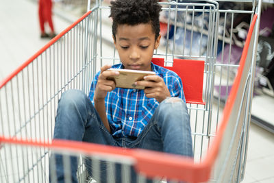 Rear view of boy using mobile phone while sitting on railing