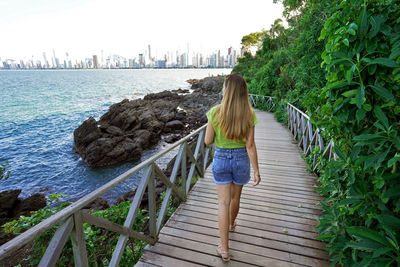 Full length of beautiful woman walking on footpath around the bay of balneario camboriu city, brazil