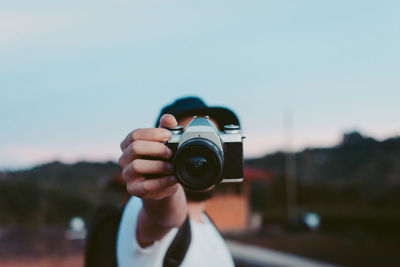 Close-up of hand holding camera against sky