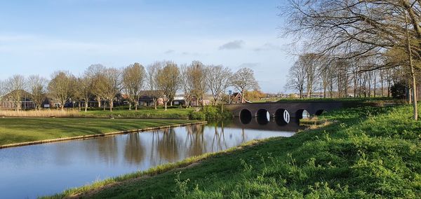 Scenic view of canal by trees on field against sky