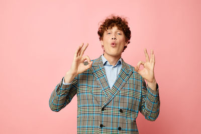 Portrait of young man standing against pink background