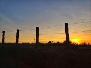 Silhouette fence on field against sky during sunset