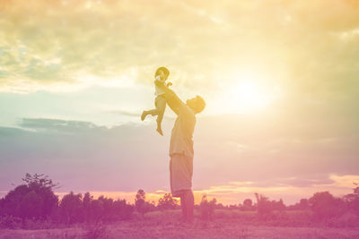 Low angle view of girl holding umbrella on field against sky during sunset