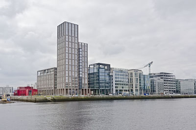 Modern buildings by river against sky in city