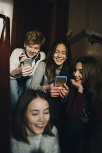Happy teenage boy with female friends using mobile phone while sitting on steps