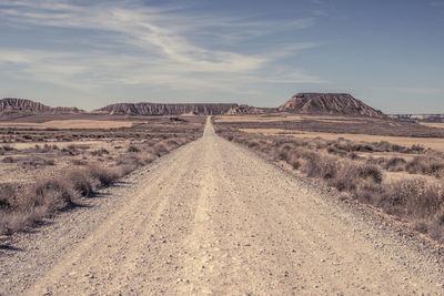 Dirt road amidst land against sky